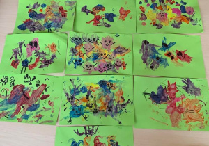 Plastykoterapia w grupie 1. Zdjęcie przedstawia prace dzieci. Stworki emocji - na zielonych kartonach rozdmuchana farba, dorysowane buźki wyrażające różne emocje.